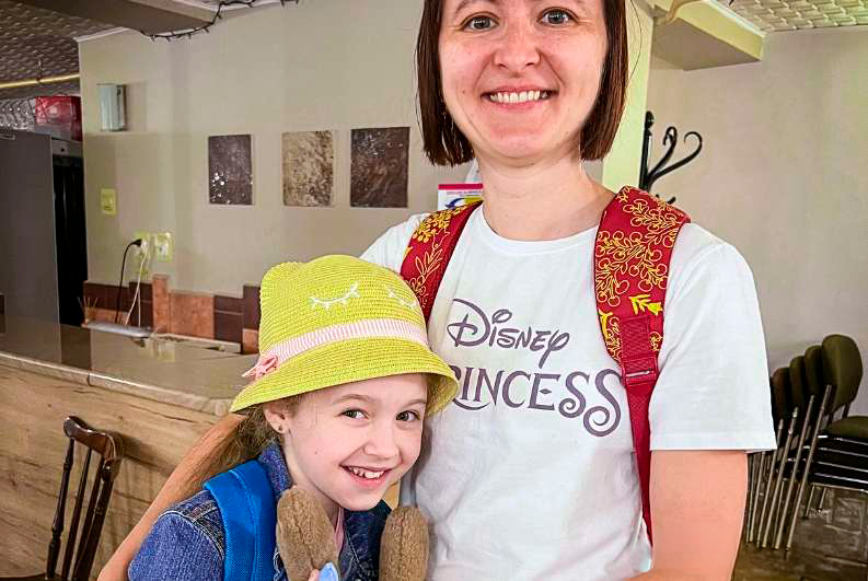 Two smiling children wearing hats and a woman posing together indoors.