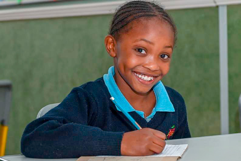 Smiling young student completing a worksheet at a classroom desk.